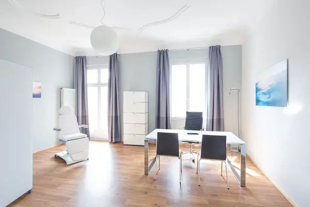 Seomra comhairliúcháin geal le deasc agus tolg cóireála ag Weight Doctors® i bhFrankfurt am Main