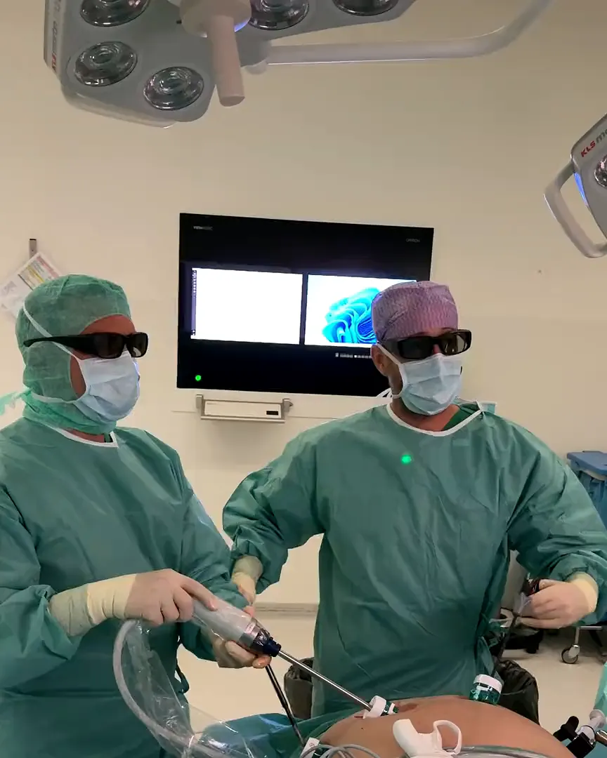 Two surgeons wearing 3D glasses operating by keyhole technique, with the monitor behind them